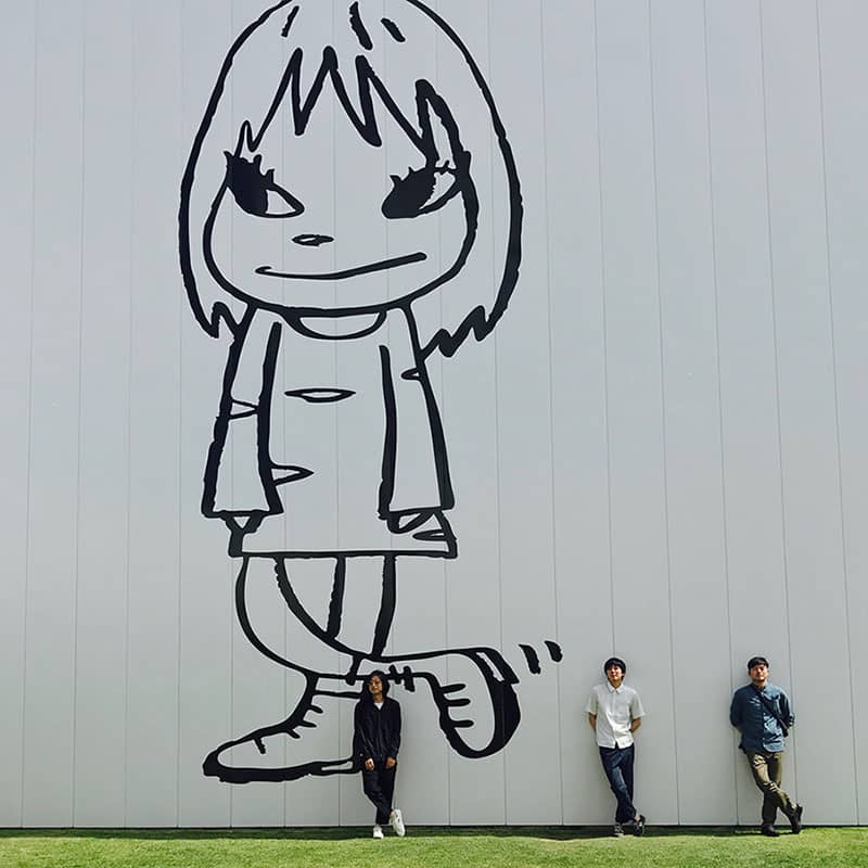 壁に描かれた女の子の絵の前で立っている3人の写真